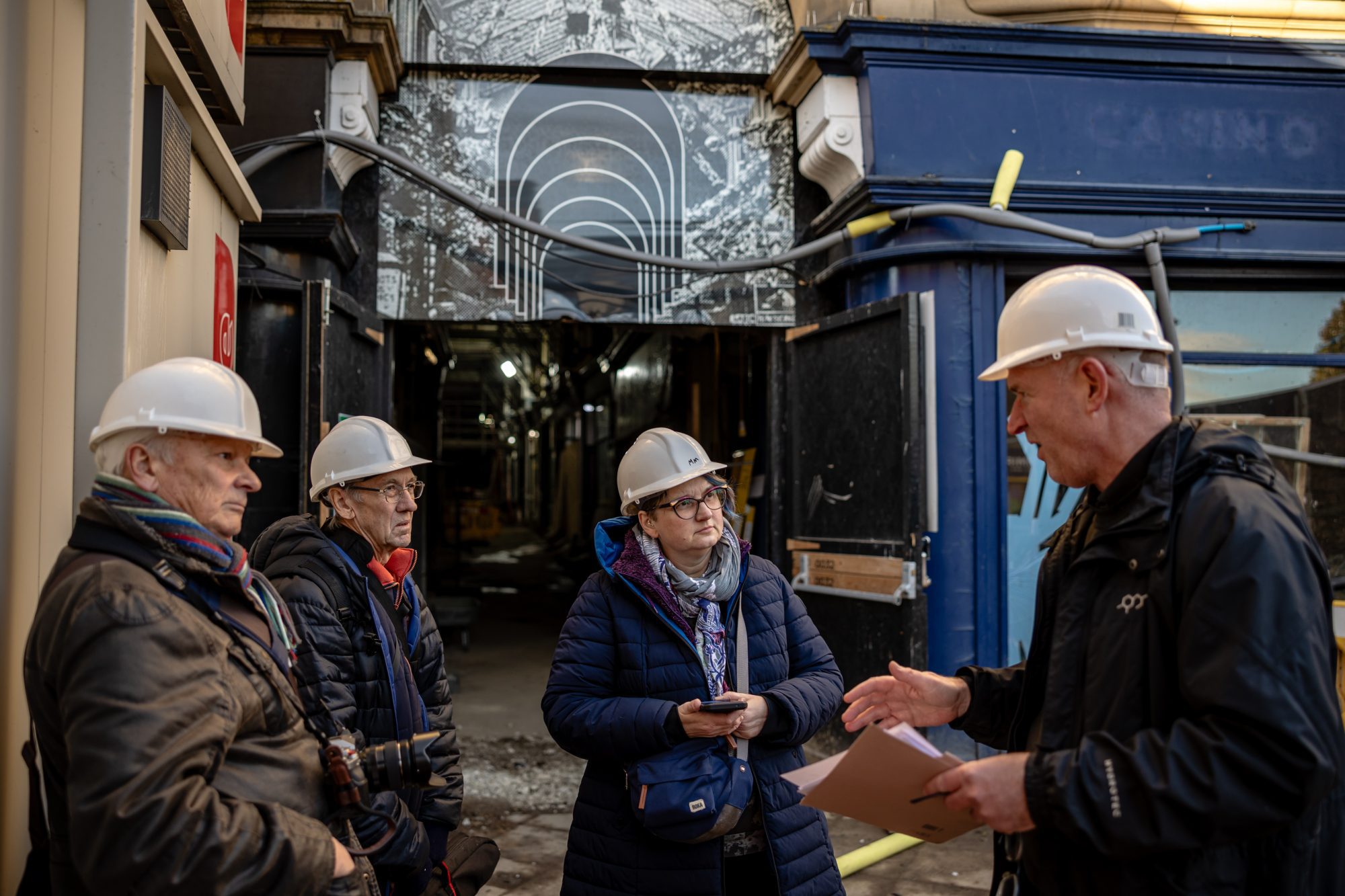 A group of people in hard hats talk outside the construction site of Dewsbury Arcade